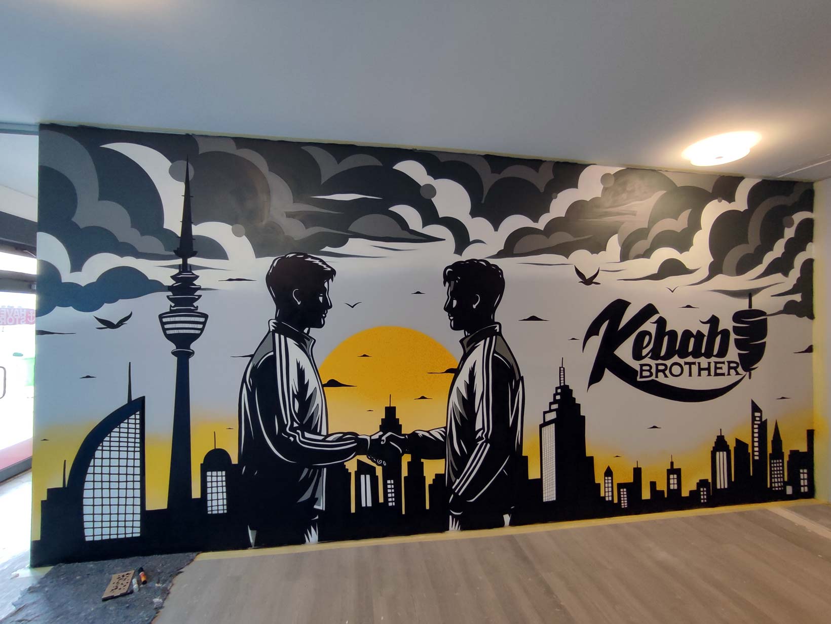 Graffiti-Wandgemälde mit zwei Männern, die sich die Hand reichen, vor einer Skyline mit Bremerhavener Gebäuden, stürmischen Wolken und einem gelben Sonnenuntergang.