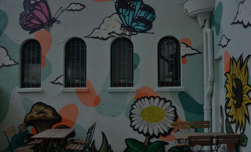 Auftrags-Graffiti für das Bio-Restaurant Seidenspinner in Oldenburg mit Schmetterlingen, einer Sonnenblume, Pilzen und Wolken im Hintergrund, umgeben von grafischen Formen.